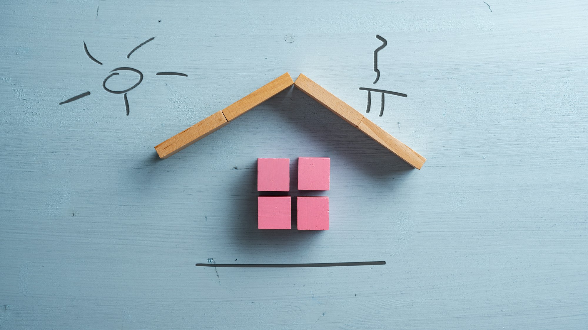 A house made of pink wooden blocks with a hand drawn chimney and sun above it