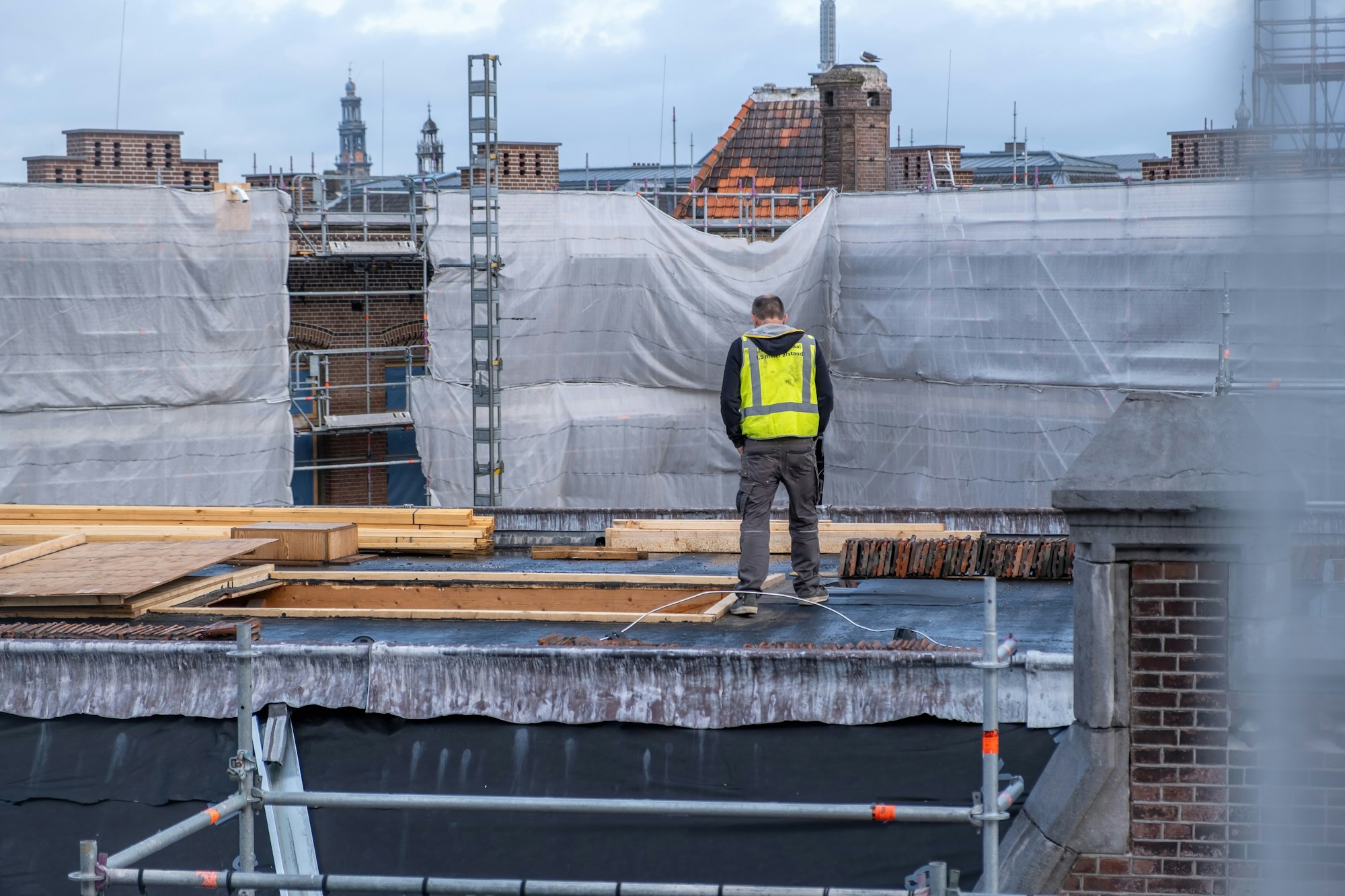 Building roof construction insulation works. Worker with yellow vest at rooftop, metal scaffolding